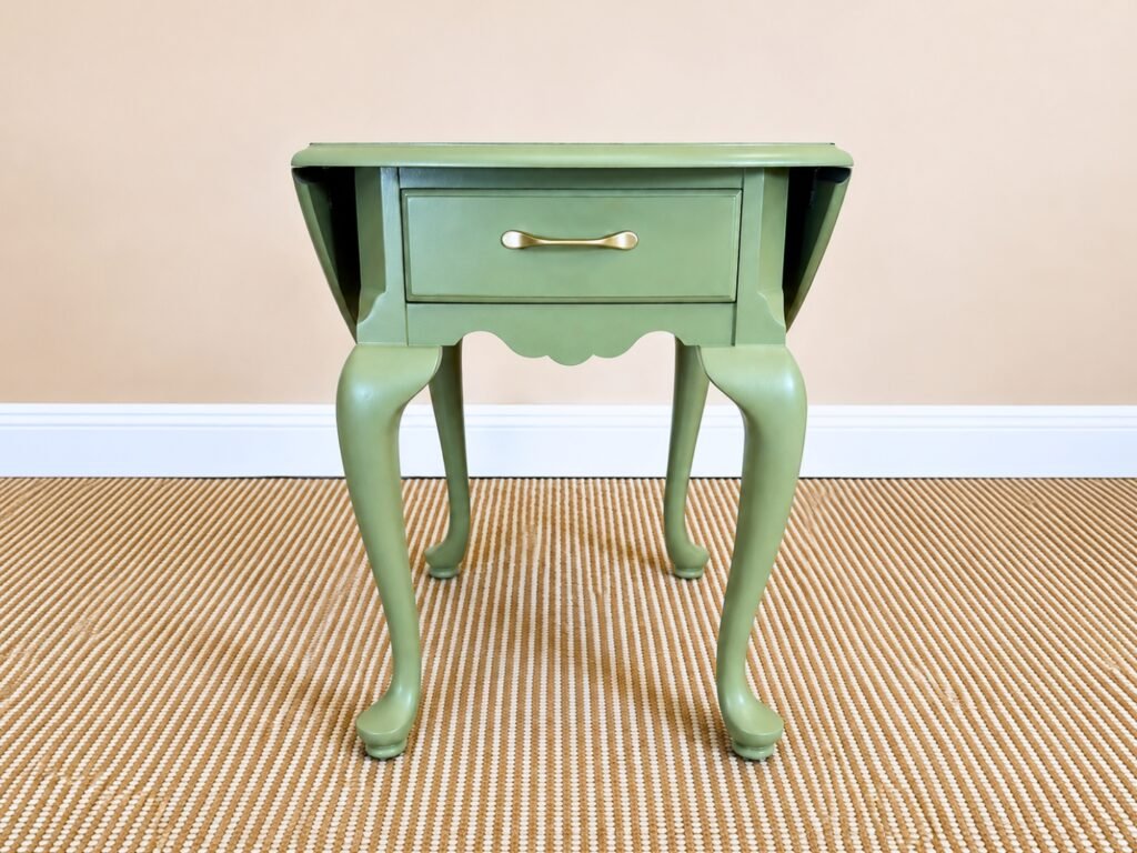 Sage green drop-leaf side table with natural wood top and brass drawer pull.